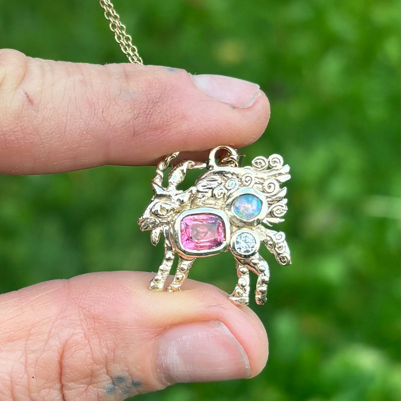 Gold goat-shaped pendant with gemstones held by a hand against a green background