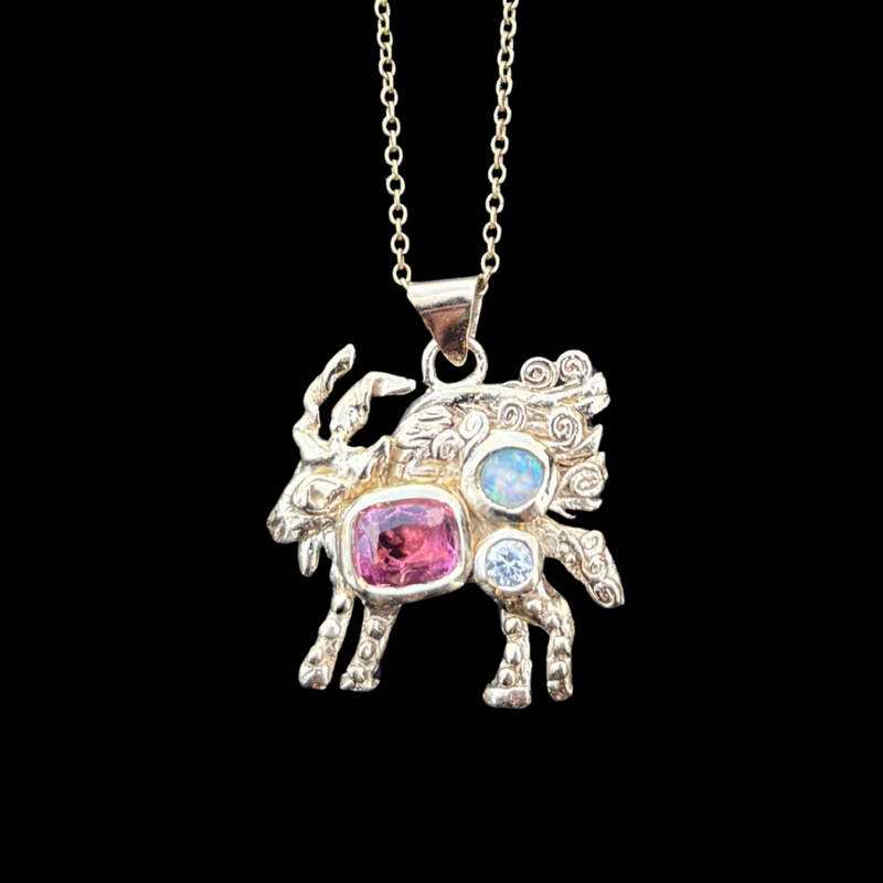 Gold goat pendant with gemstones on a chain against a black background
